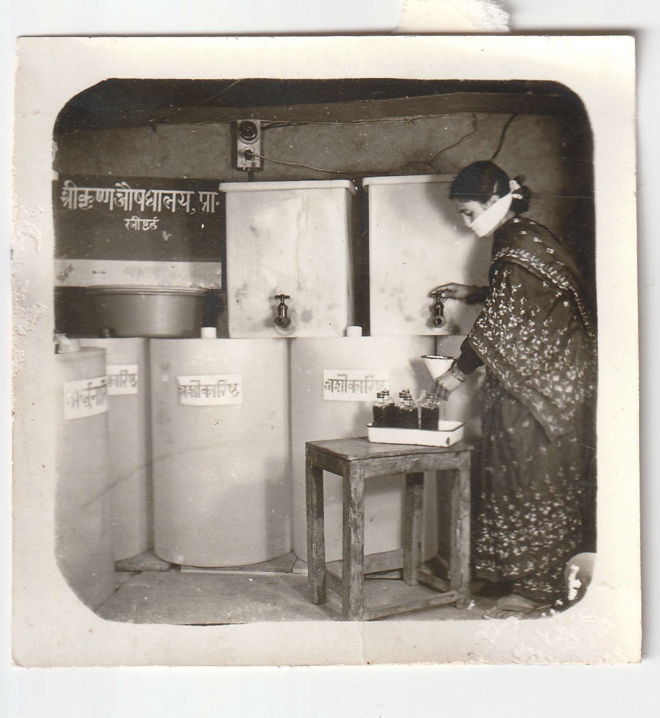 Filling glass bottles from preparation vessels carrying the label अशोकारिष्ट. Date unrecorded.
